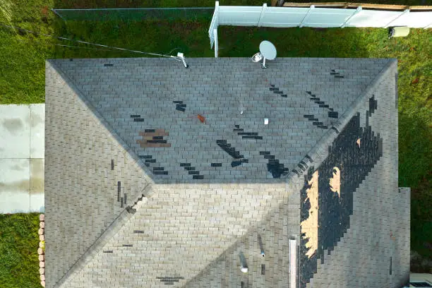 Photo of Wind damaged house roof with missing asphalt shingles after hurricane Ian in Florida. Repair of home rooftop concept