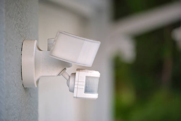 Motion sensor with light detector mounted on exterior wall of private house as part of security system.