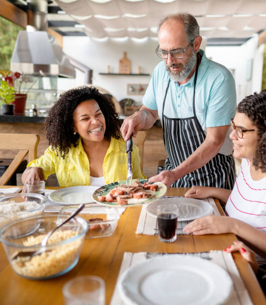 Mature man serving food during a barbecue in summer Mature man serving his daughter's friends food while sitting around an outdoor table during a barbecue brazilian bbq stock pictures, royalty-free photos & images