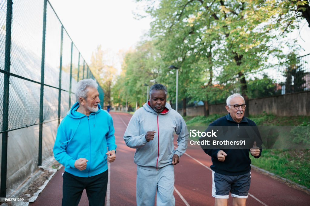 Diverse active seniors doing jogging workout on outdoor sports court Diverse active seniors doing jogging workout on outdoor sports court. Multiracial senior male friends running together on exercise track. Active Lifestyle Stock Photo