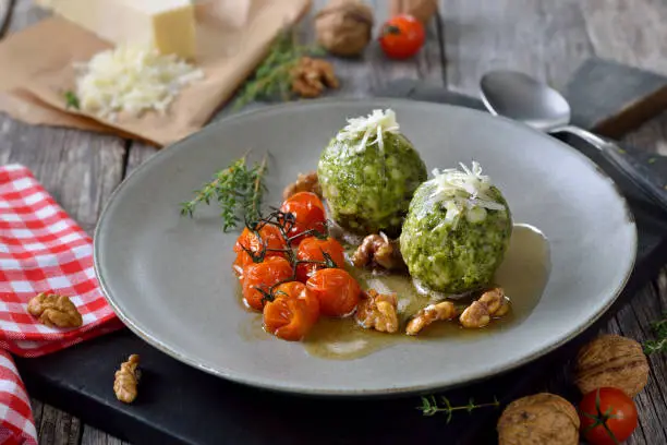 Homemade traditional South Tyrolean spinach dumplings made of white bread and fresh spinach leaves, served with browned butter, baked cherry tomatoes, walnuts and grated parmesan cheese