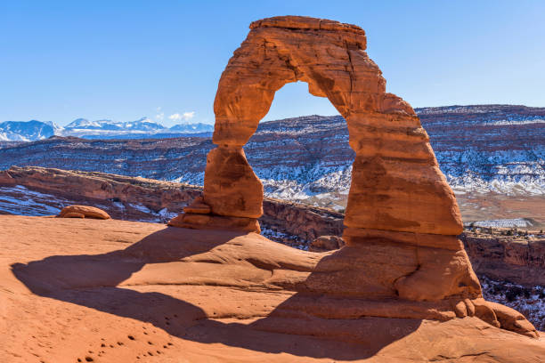 winter delicate arch - a closeup view of delicate arch, with snow-covered la sal mountains towering in background, on a clear sunny winter day. arches national park, utah, usa. - mountain range utah sky mountain imagens e fotografias de stock