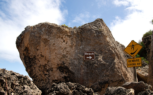 Large rock at Stokes Beach in Kangaroo Island, South Australia with sign to the beach and sign warning of strong rip.