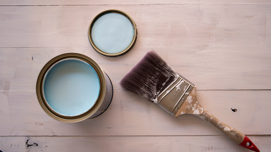 Paint brush on paint can with partially painted timber surface in the background