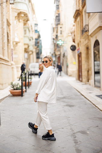 Young fashionable woman in white suit posing in old town