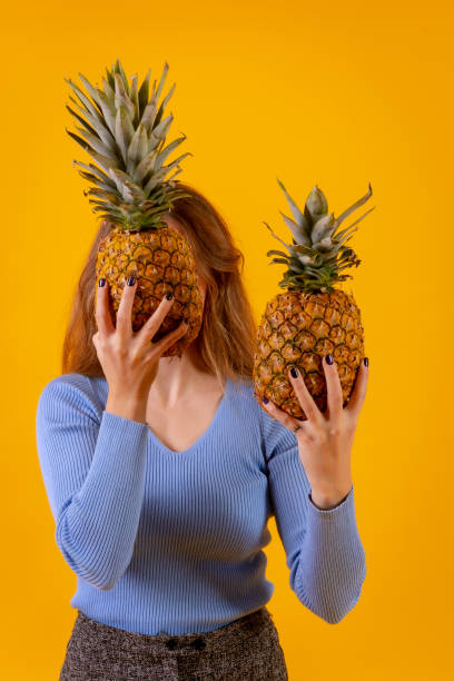 istock pineapple cut in half, yellow background, behind a woman holding it 1452787584