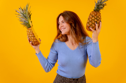 Vegetarian woman with a pineapple in sunglasses, dancing and happy, healthy life, yellow background