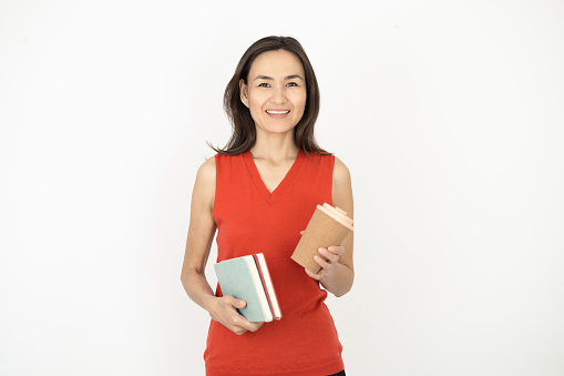 Studio portrait of a beautiful Asian woman holding books and a coffee cup
