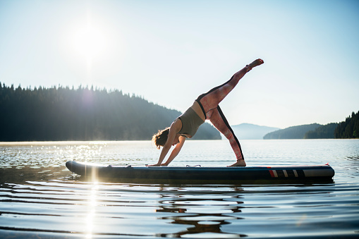 Tranquil scene of woman doing yoga on paddleboard.