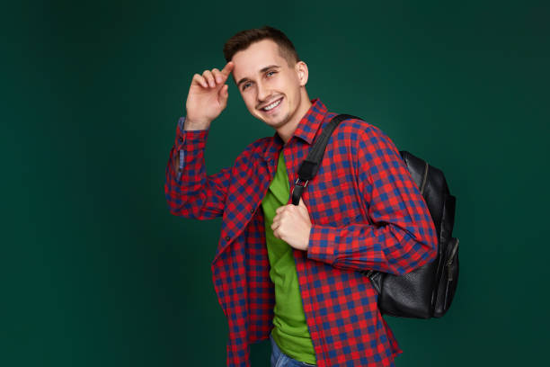 cheerful handsome man in red plaid shirt with backpack looking at camera on green background