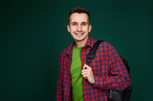 smiling handsome man in red plaid shirt with backpack looking at camera on green background. copy space