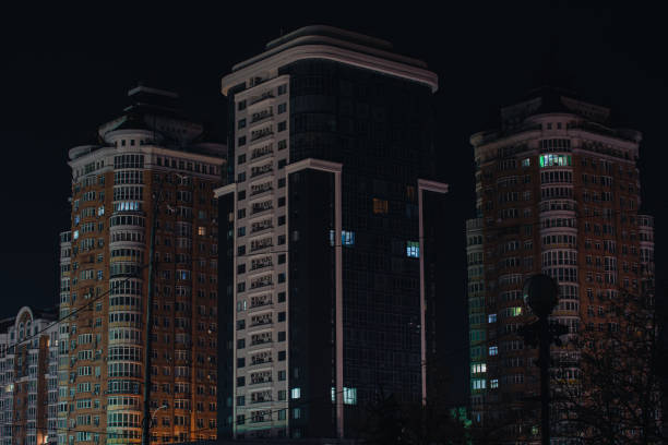 Facade of a modern apartment building in blackout. Some windows lights up in the house. Apartment building without electricity at night