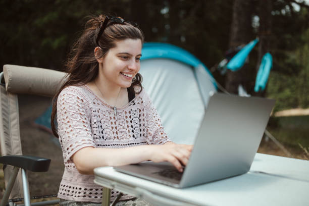istock Smiling young woman using laptop on camping vacation for working remotely. 1452790264