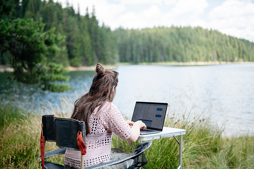 Young woman working with laptop during her camping vacation in mountain.Balancing between leisure and work.