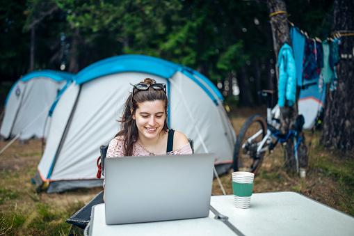 Smiling woman using laptop during camping in the mountains.