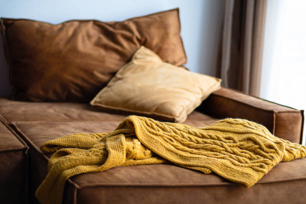 A yellow knitted plaid lies on a sofa with pillows. Home interior.