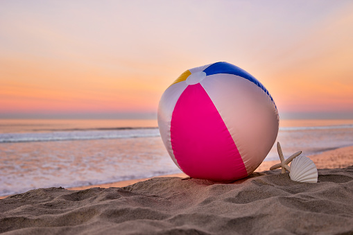 This is a close up photo of a beach ball at sunrise sitting on the sand with the ocean in the background