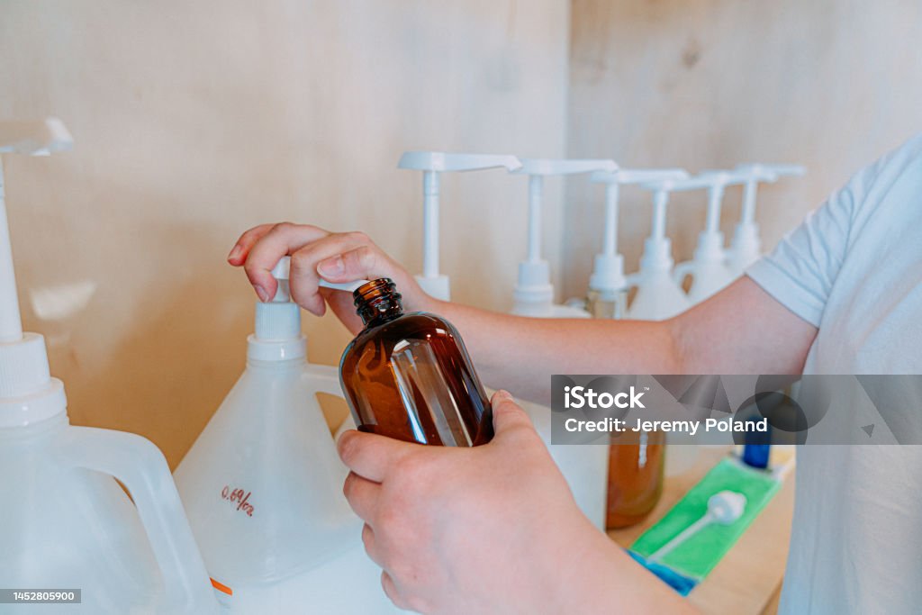 Young Woman's Hands Pumping Shampoo or Body Wash from a Bottle, Making Sustainable Choices at a Plastic-Free Retail Store A young woman is seen making sustainable choices at a plastic-free retail store. She is holding a reusable container and is closely examining a shelf of beauty products, including shampoo, shower gel, and soap. 

The store, which is focused on environmental conservation and ethical consumerism, is filled with a variety of sustainable products, including reusable items and recycled materials. The woman, who is representing a zero waste lifestyle and a healthy lifestyle, is making a conscious decision to shop with the planet in mind. 

This photo is suitable for use in a variety of contexts, including retail, consumerism, domestic life, and social issues related to environmental and environmental issues. It is part of a series that highlights the importance of individual choice and responsibility in promoting sustainable living and the protection of planet Earth. Refill Stock Photo