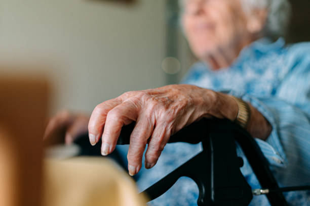 Close-Up Shot of a Caucasian Senior Woman Resting Her Hand on the Grip of her Mobility Walker while Sitting and Looking Out the Window stock photo
