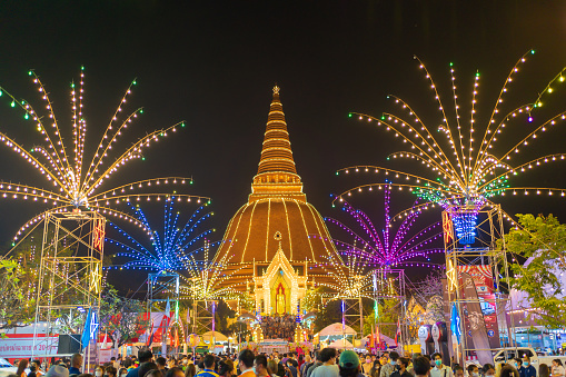 Street food festival market in Phra Pathommachedi temple at night. The golden buddhist pagoda with residential houses, urban city of Nakorn Pathom district, Thailand. Holy Thai architecture.