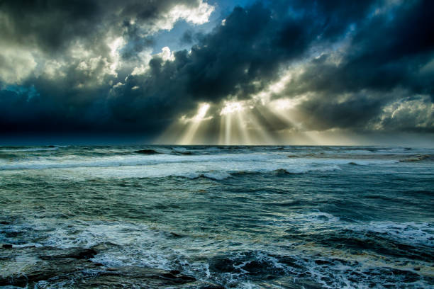 Beams of light in the midst of a dark storm over the coast at Muriwai beach