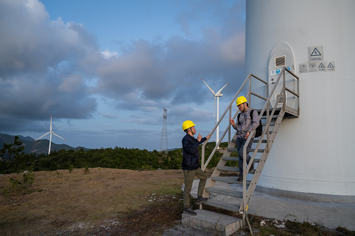 Two male engineers work in the mountain wind power station