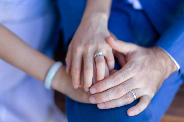 istock The bride wears a Chinese jade bangle. She is showing off her diamond ring with a groom wearing an engagement ring nearby holding her hand. 1452826321