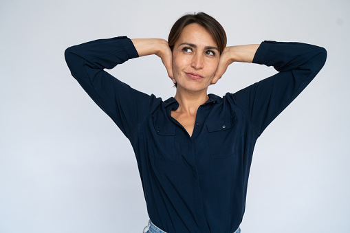 Uninterested woman covering ears. Female model in dark blue shirt not listening to something, looking aside. Portrait, studio shot, nonchalance concept
