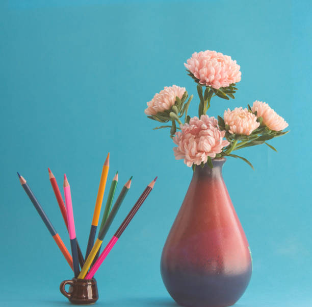 buket bunga aster merah muda dalam vas dan pensil warna dalam cangkir. konsep ide kreatif seni, latar belakang biru. - vas pencil potret stok, foto, & gambar bebas royalti