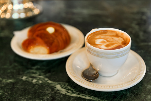 Cup of cappuccino and a cornetto, Italian croissant with cream at breakfast on a counter at a cafe in Centro Storico, Florence, Italy