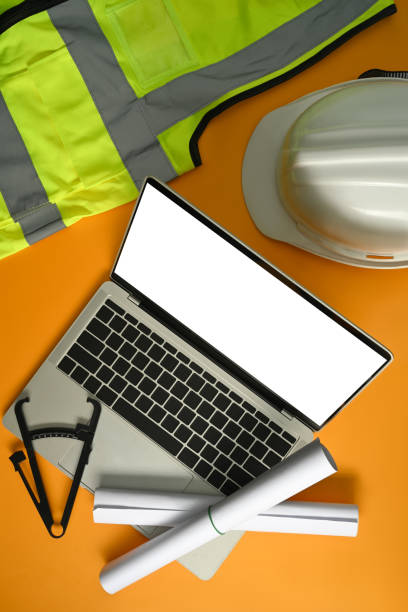 istock Laptop computer, blueprints, safety hardhat, coffee cup and stationery on yellow background. 1452832718