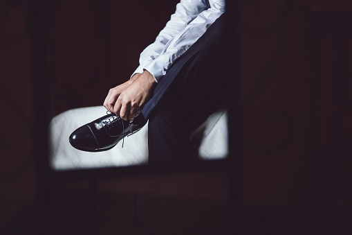 A man sitting on the bed and lacing up his leather shoes on his wedding day