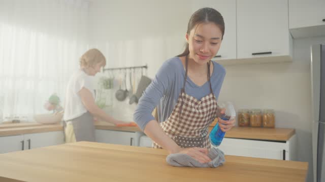 Caucasian senior elderly woman cleaning kitchen in house with daughter. Attractive female housekeeper and mature cleaner wear apron, feel happy and relax while working for housework or chores at home.