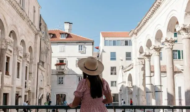 A back shot of a Caucasian female tourist admiring the Peristyle in Diocletian's Palace on a sunny day in Split, Croatia.