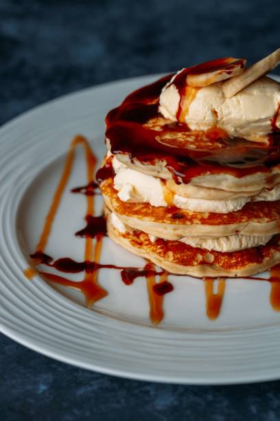 Vertical shot of pancakes with cream and bananas on a white plate