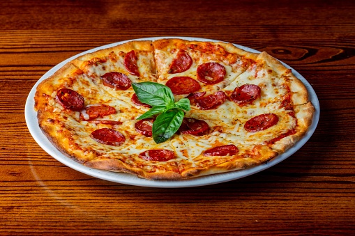 A close-up shot of a classic pepperoni pizza served with basil leaves.
