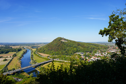 View of the landscape and the Weser from the Porta-Kanzel in Porta Westfalica. Green nature with a river, fields, hills and the Kaiser Wilhelm monument.