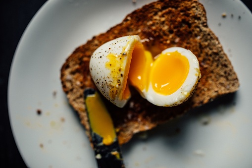 jammy soft boiled egg on whole wheat toast with salt, pepper, knife
