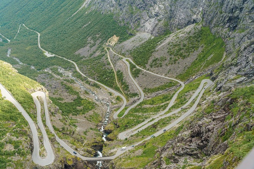 An aerial view of mountain road with cars in drive surrounded by greenery trees and bushes