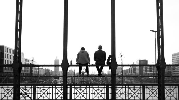 istock Grayscale shot of two people sitting on a bride railing 1452850340
