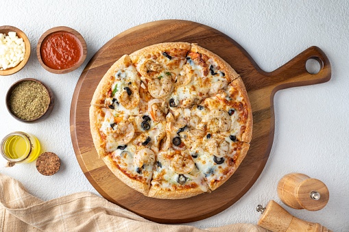 A top view of a tasty seafood pizza with shrimps, tomato sauce, and cheese on a wooden board