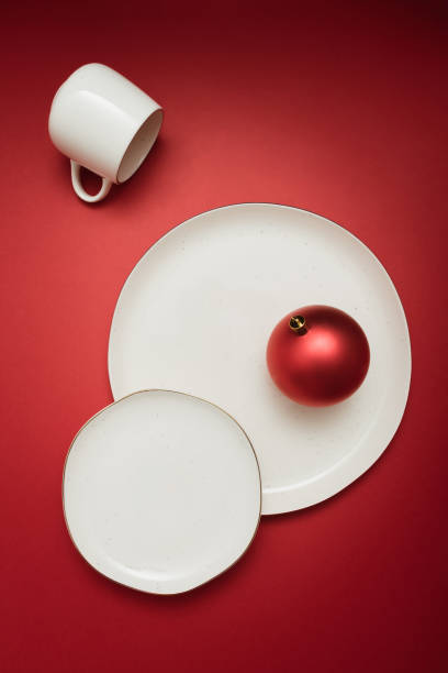 istock Creative table setting with two plates, a cup and bright red christmas bauble on red background. Minimal celebration idea. 1452851218