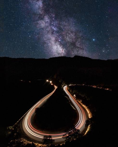 istock Curvy road with car trails in long exposure under a starry night sky 1452851999