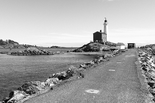 A grayscale shot of a pier leading to the lighthouse in spring