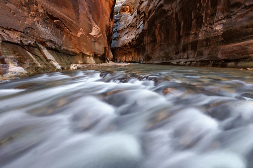 A small waterfall across the Virgin River beneath the red cliffs near the Temple of Sinawava along the Riverside Walk in Zon National Park, Utah.