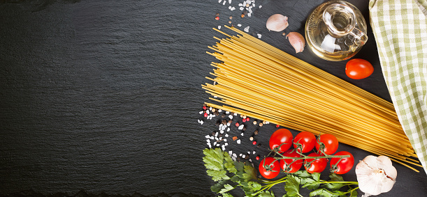 Pasta, spaghetti and cooking ingridients on black slate surface. Italian cuisine concept, restaurant menu, recipe template. Top view, flat lay, mockup, banner, header with copy space for text