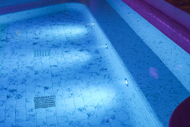 A luxury swimming pool with lighting in night. A luxury swimming pool with clearly transparent water and white marble tile floor. Building place photo, selective focus at marble tile. Photo contained some noise due to low light environment. pond stock pictures, royalty-free photos & images