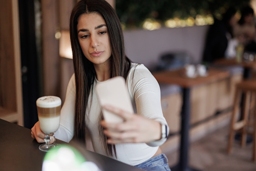 Beautiful young woman taking selfie with coffee cup to share on social media