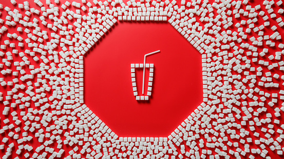 octagonal frame in the form of a stop sign made of sugar cubes with red background and glass outline with a straw inside. stop eating refined sugar concept