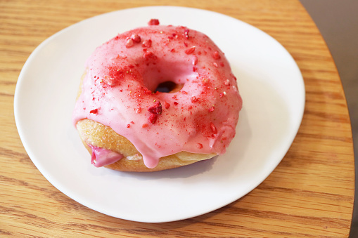 Delectable strawberry-glazed with raspberry cream filling doughnut on a white plate